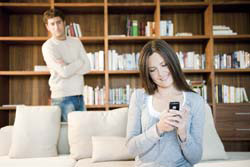 woman using cell phone and husband is watching