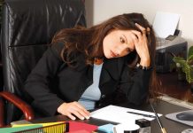 Female Executive stressed out and sitting at her desk massaging her head to relieve a tension headache