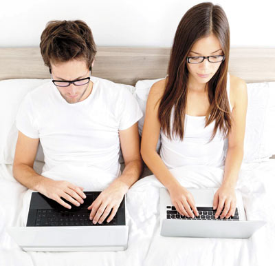 Husband and wife working on their respective laptops in bedroom