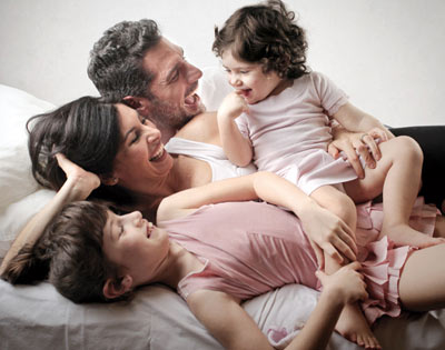 Happy family laughing on bed with two kids