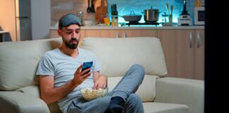 This is Normal — Man Sitting on Couch with a Bowl of Popcorn in Hand, Immersed in the Phone