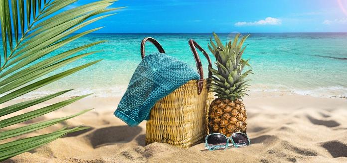 a basket, a pineapple and sun shades lying on beach sand