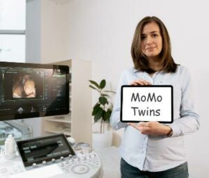 Pregnant woman near ultrasound machine holding a placard of MoMo Twins