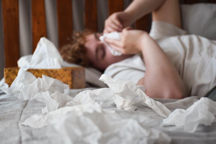 Man suffering from extreme nasal congestion on bed with tissues