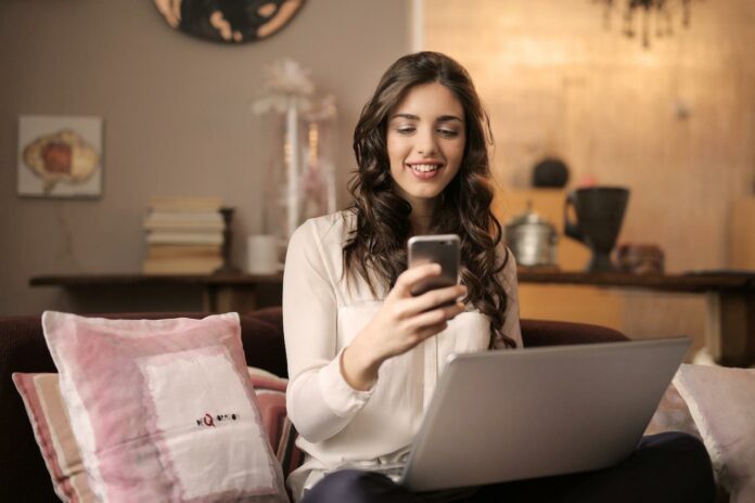 Beautiful smiling young woman sharing information with smartphone and laptop